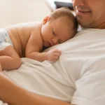 Pai segurando o bebê no colo enquanto dorme nos primeiros meses de vida