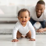 bebê engatinhando e sorrindo o pai observa os saltos de desenvolvimento do bebê.